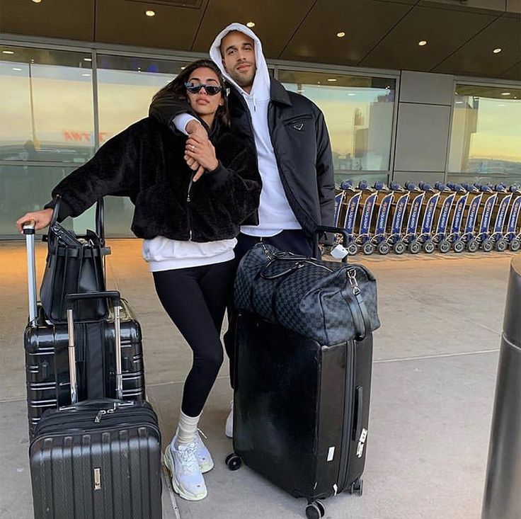 a man and woman standing next to each other with luggage in front of an airport