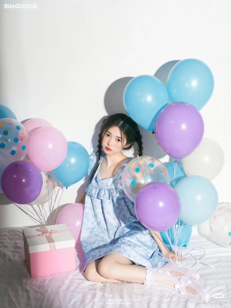 a woman is sitting on a bed with balloons and presents in front of her as she poses for the camera