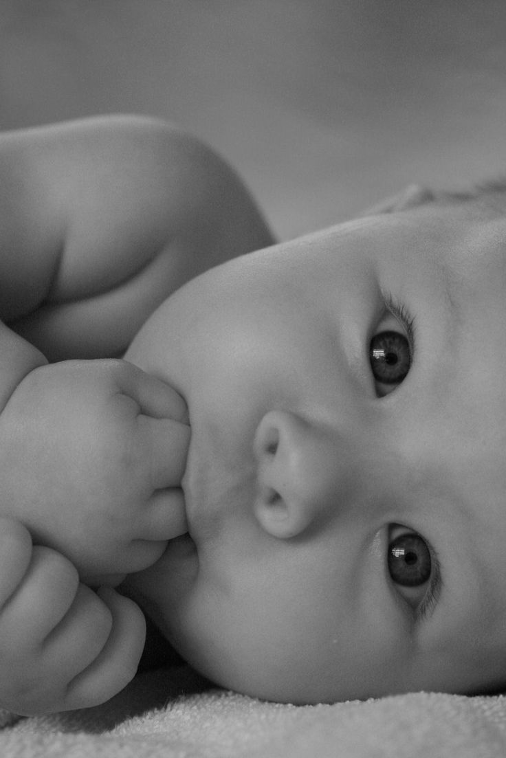 a black and white photo of a baby laying on it's back with its head up