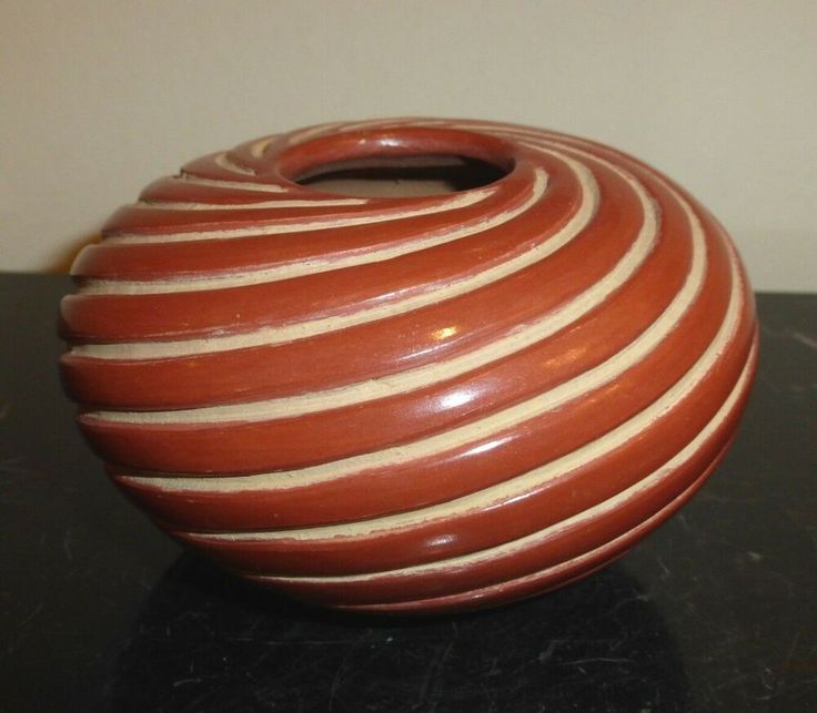 a brown and white striped vase sitting on top of a black table next to a wall