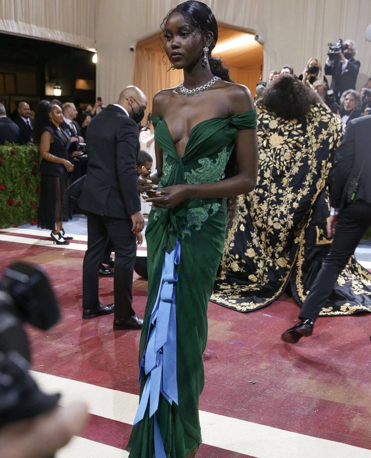 a woman in a green and blue dress standing on a red carpet with cameras around her