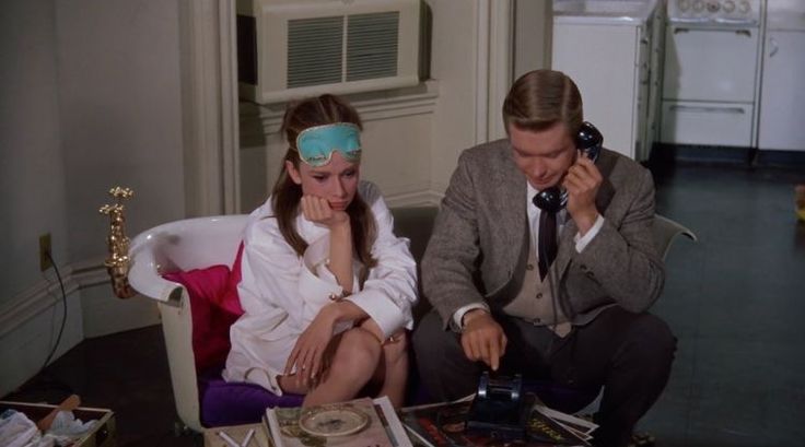 a man and woman sitting on a couch talking on cell phones while one holds a telephone to her ear