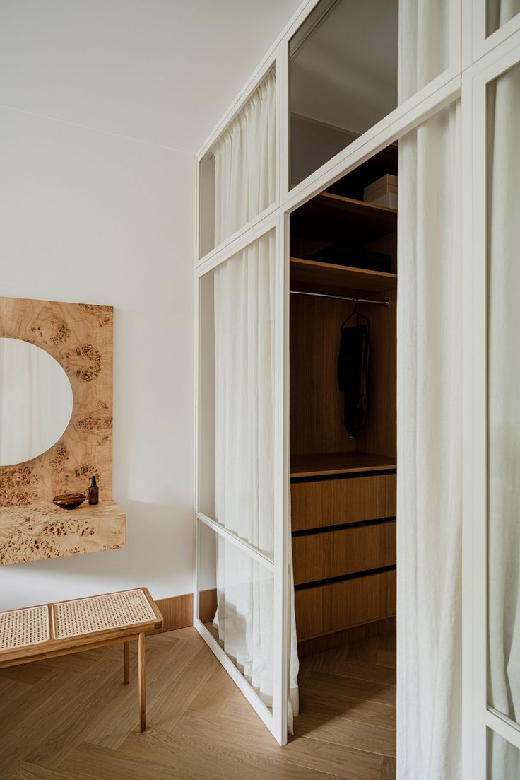 an open closet with white curtains and a wooden bench in the foreground, next to a large mirror