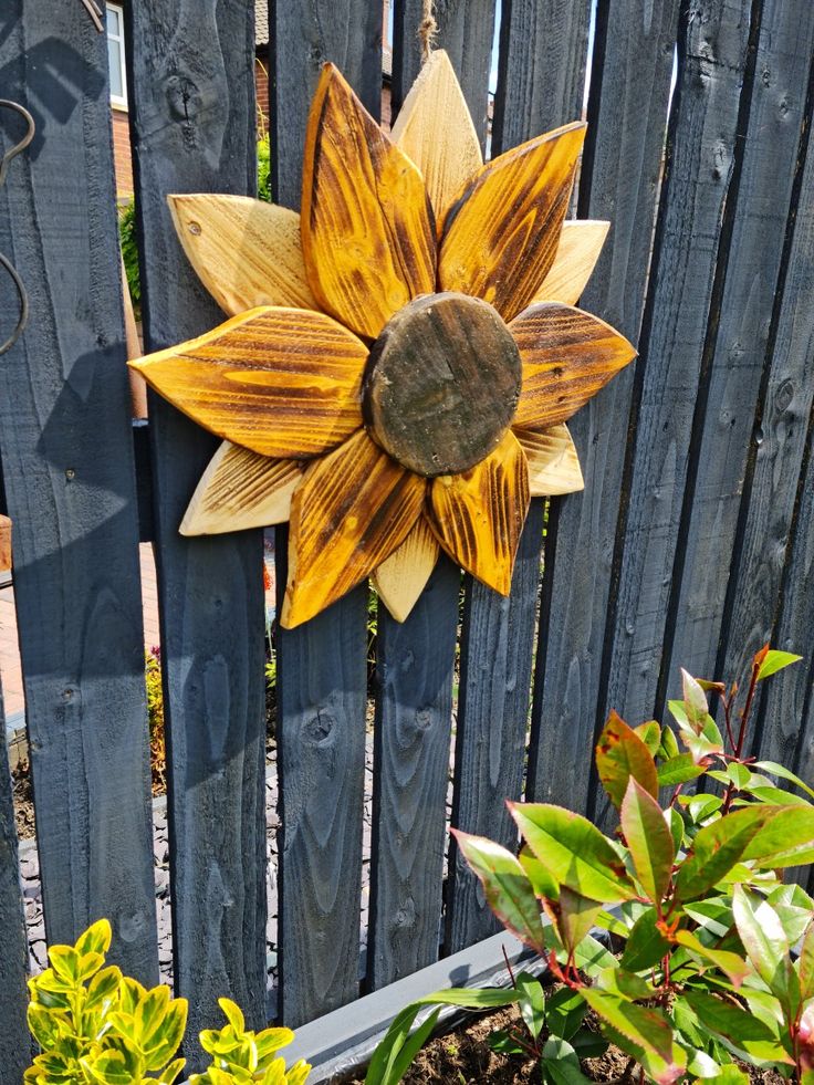 a wooden sunflower sitting on the side of a fence