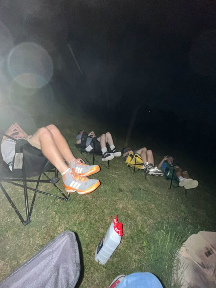 people are sitting in chairs on the grass at night with their feet propped up against each other