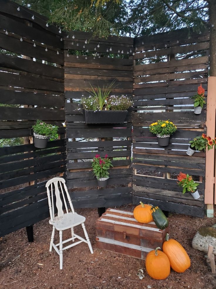 a white chair sitting in front of a wooden fence with potted plants on it