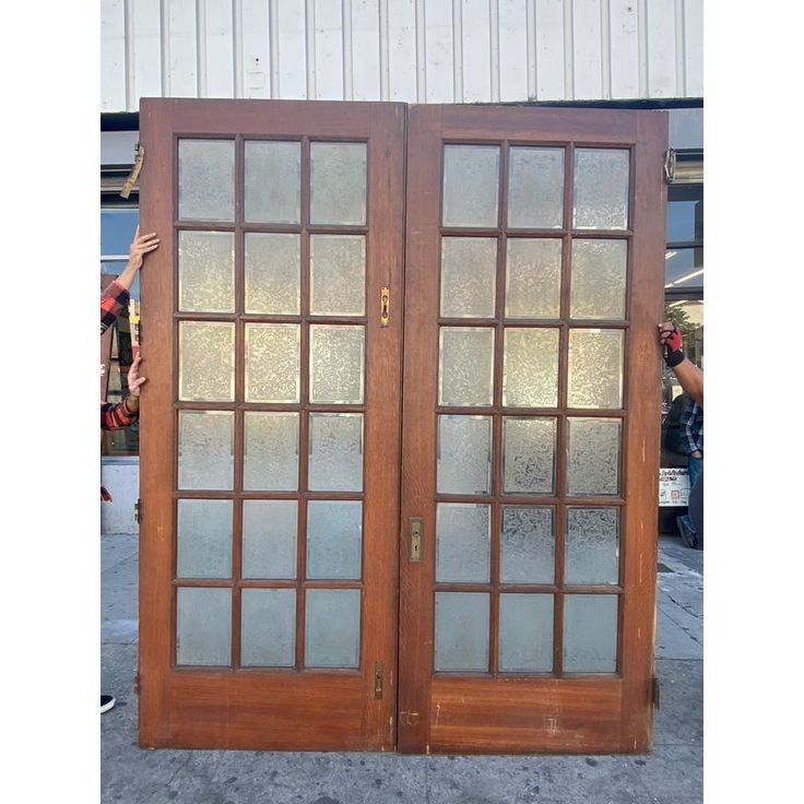 two wooden doors with frosted glass on the top and bottom, in front of a building