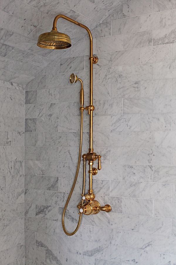 a shower head and hand shower in a white bathroom with marble tile on the walls