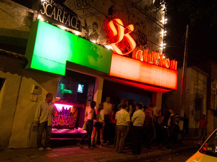 a group of people standing in front of a neon sign on the side of a building