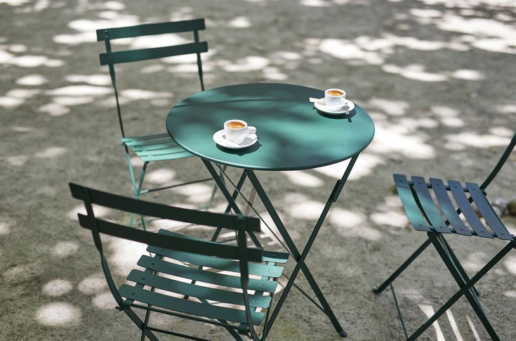 two chairs and a table with cups of coffee sitting on them in the middle of a park