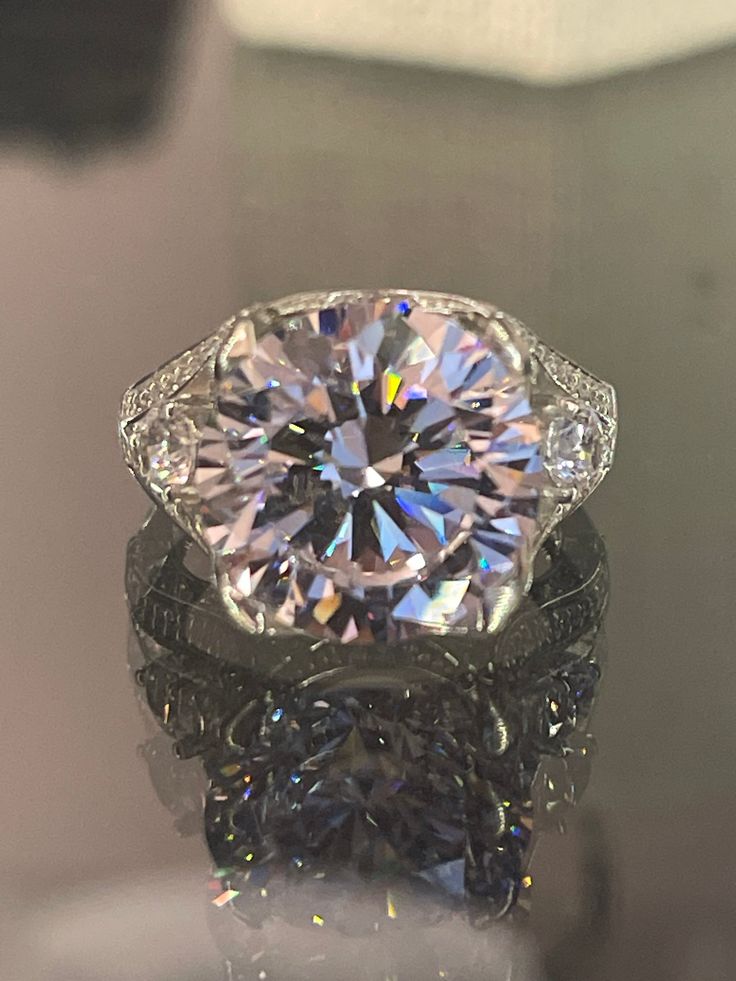 a fancy diamond ring sitting on top of a glass table with its reflection in it