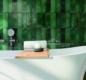 a bathtub with green tiles on the wall behind it and a wooden tray in front of it