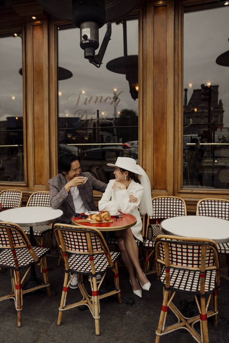 A couple taking pre-wedding photos in classic style in front of a café in Paris. Paris Apartment Photoshoot, Couples Photoshoot In Paris, Prewedding Cafe, Apartment Photoshoot, Cafe Couple, Couples In Paris, Nyc Shoot, Cafe Photoshoot, Paris Mood Board