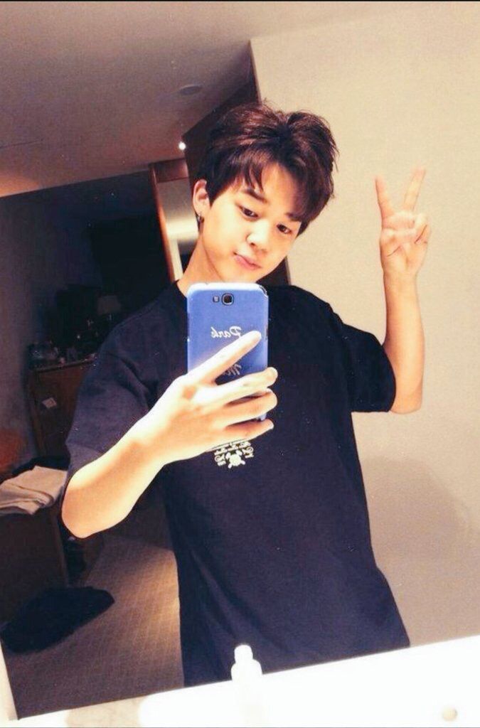 a young man standing in front of a mirror looking at his cell phone and making the peace sign