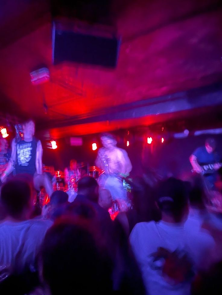 a group of people that are standing in front of a bar with red lights on the ceiling