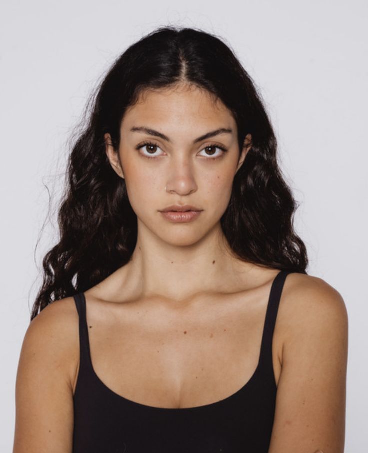 a woman with long dark hair wearing a black tank top and looking at the camera