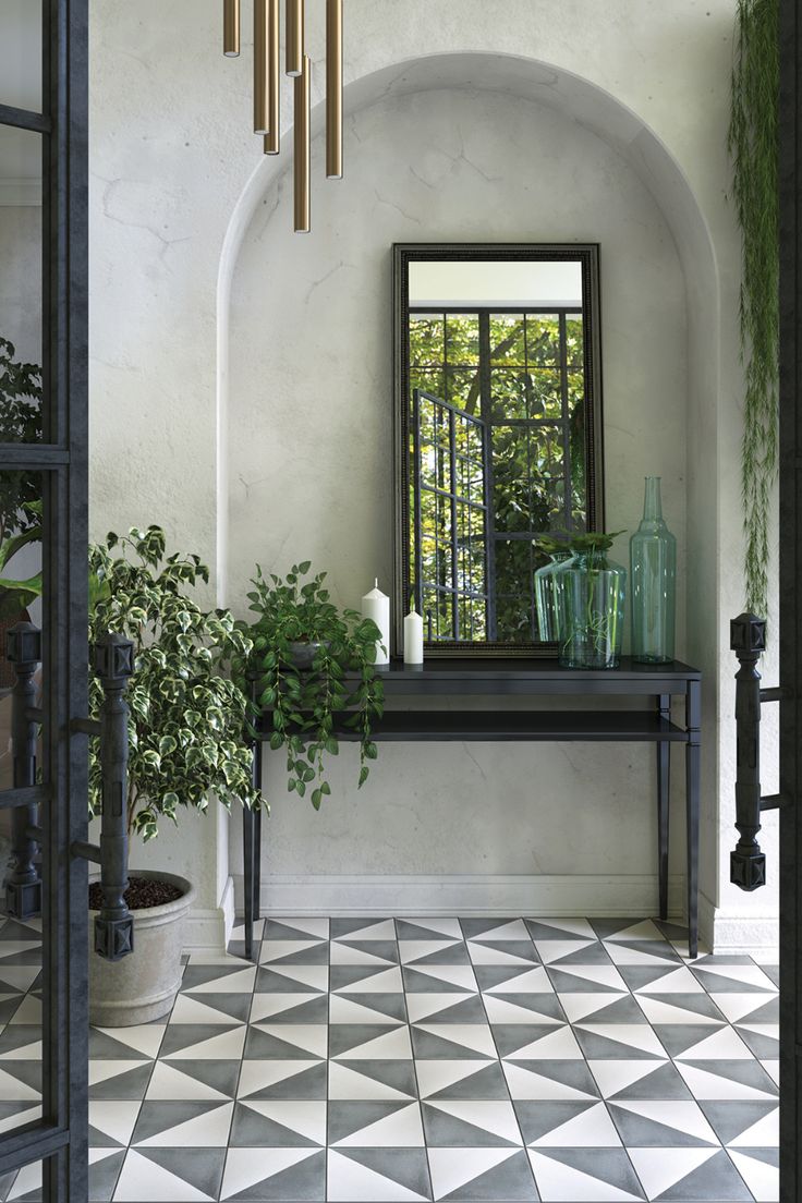 an entryway with black and white tiled flooring, potted plants and mirrors