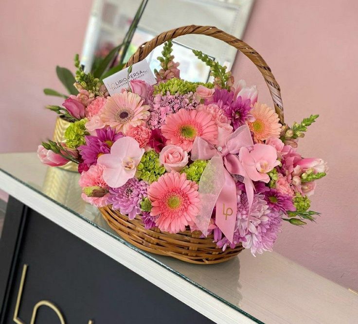 a basket filled with pink flowers sitting on top of a counter next to a mirror