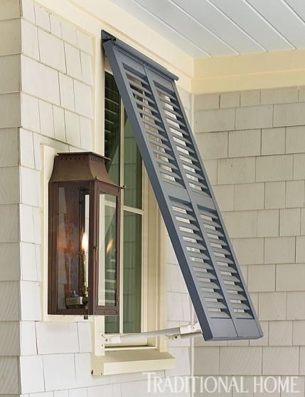 an open window on the side of a house with shutters and a lamp in it