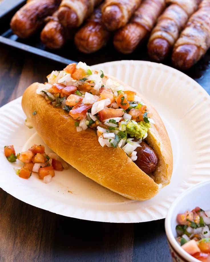 a hot dog on a paper plate next to some sausages and condiments