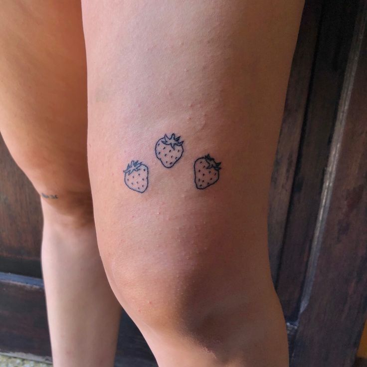 a woman's legs with three strawberries tattoo on her left calf and the other half of her leg