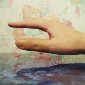 a person's hand on top of a table with a flowered wallpaper behind it