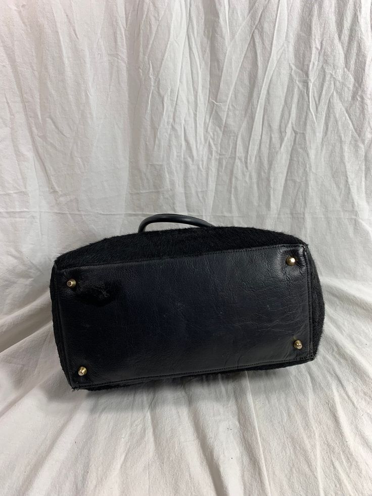 "Measurements are 14\" top wide, 10\"5 high, 5\"8 deep with two 48\" straps each side to side with a 8\" drop. On the interior there is one main compartment, unlined leather, back zipper pocket and a top magnetic closure. Bag is made of calf hair with black leather trim, gold tone hardware and chunky handles. Please note bag is not new and there are scuffs with some balding and bag is great for daily use and will last you for years to come. I WANT TO STRESS THAT THIS ITEM IS VINTAGE WHICH MEANS Luxury Black Weekender Bag With Handles, Black Leather Trim Tote Travel Bag, Black Leather Trim Travel Tote Bag, Black Travel Tote With Leather Trim, Black Travel Tote Bag With Leather Trim, Black Leather Trim Weekender Satchel Bag, Black Top Handle Bag With Leather Trim, Formal Leather Travel Bag With Handles, Chic Tote Bag With Lined Interior