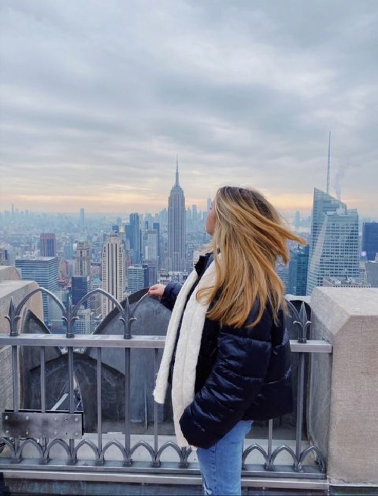 a woman standing on top of a tall building looking at the cityscape behind her