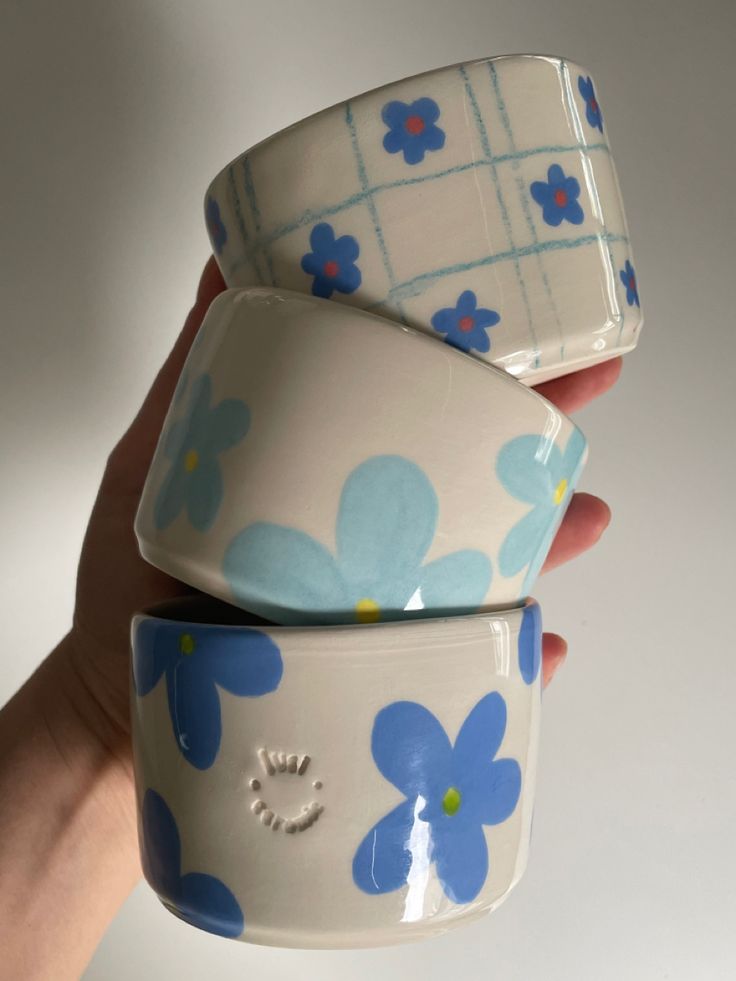 three bowls with blue and white flowers are stacked on top of each other in front of a person's hand