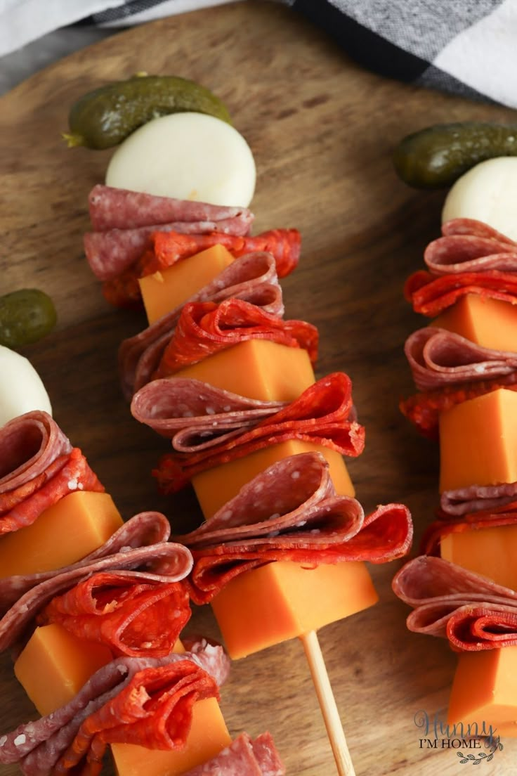 meat and cheese skewers with pickles on a cutting board for appetizers