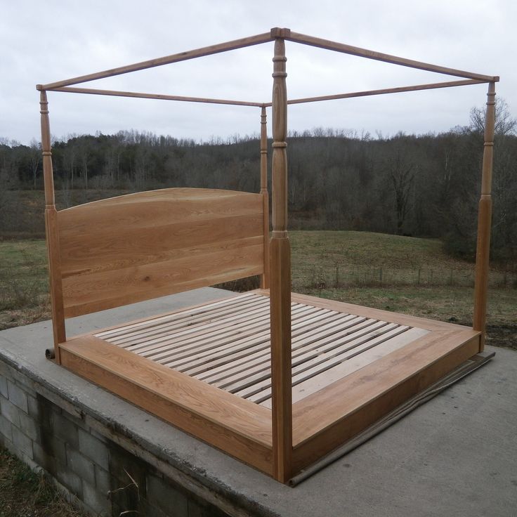 a wooden bed frame sitting on top of a cement platform in the middle of a field