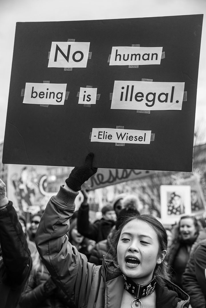 a woman holding up a sign that says no human being is illegal with other people in the background