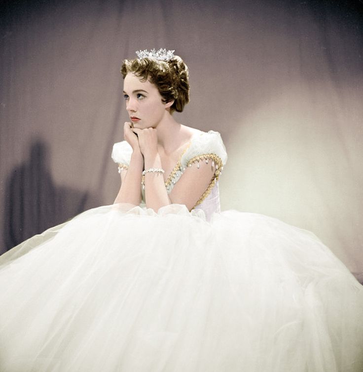 a woman in a white dress is posing for a photo with her hands on her chin