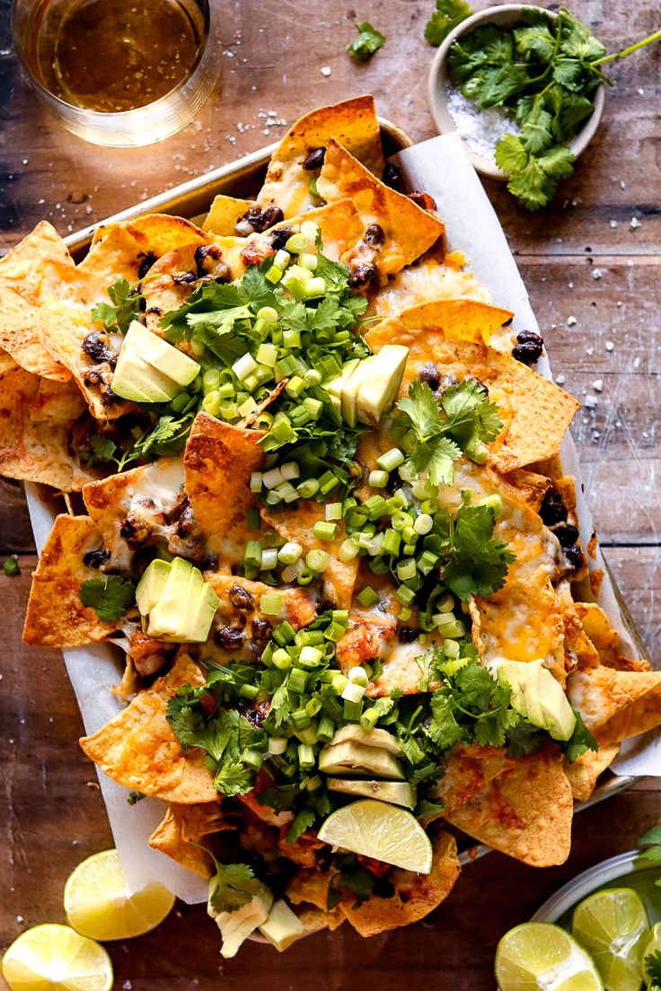 nachos on a platter with lime wedges and cilantro sauce