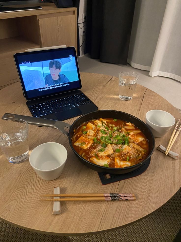 a table with a laptop, bowl and chopsticks on it