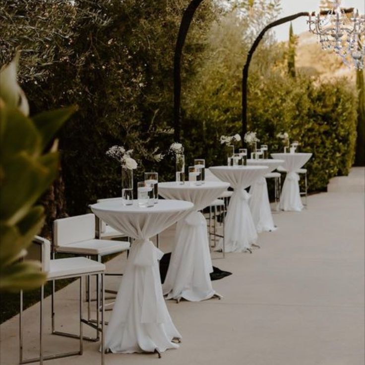 tables and chairs with white linens are lined up along the side of an outdoor walkway