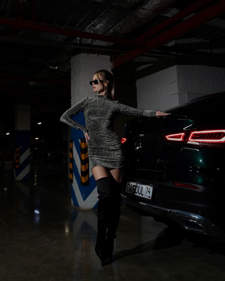 a woman standing next to a black car in a parking garage with her hands on her hips