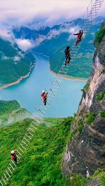 three people climbing up the side of a mountain with ladders on their feet and one person standing on top