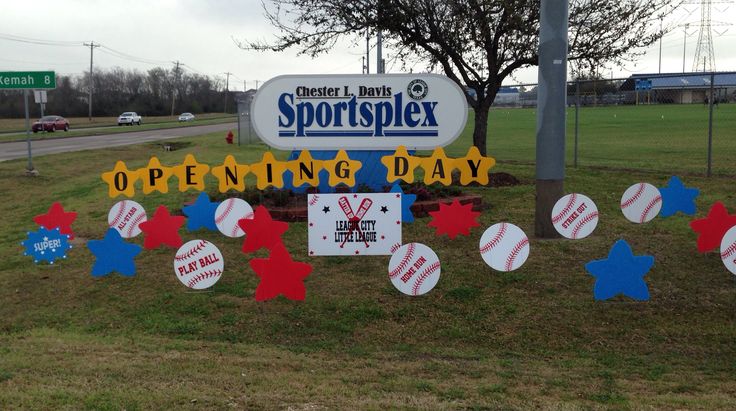 a sign that says sportsplex opening day in front of a field with baseballs and stars