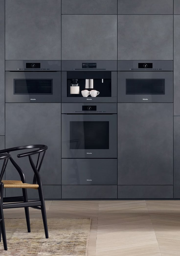 a kitchen with gray cabinets and black chairs next to a counter top oven that is built into the wall