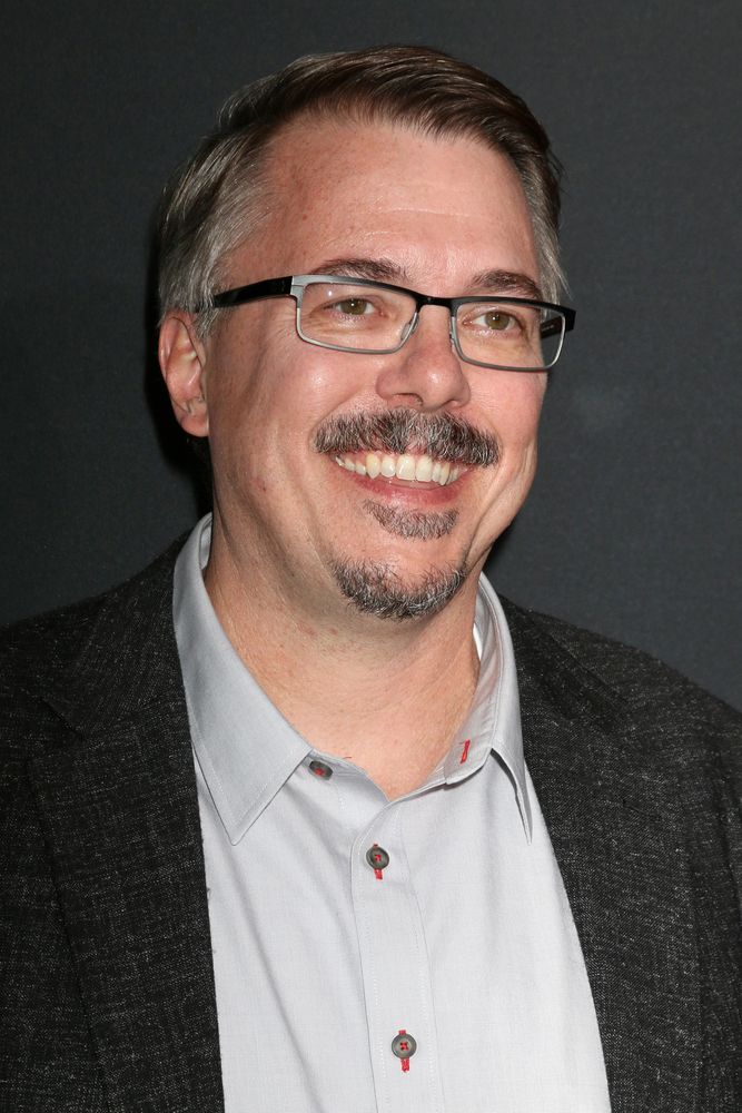 a man with glasses and a mustache smiles at the camera while standing in front of a black background