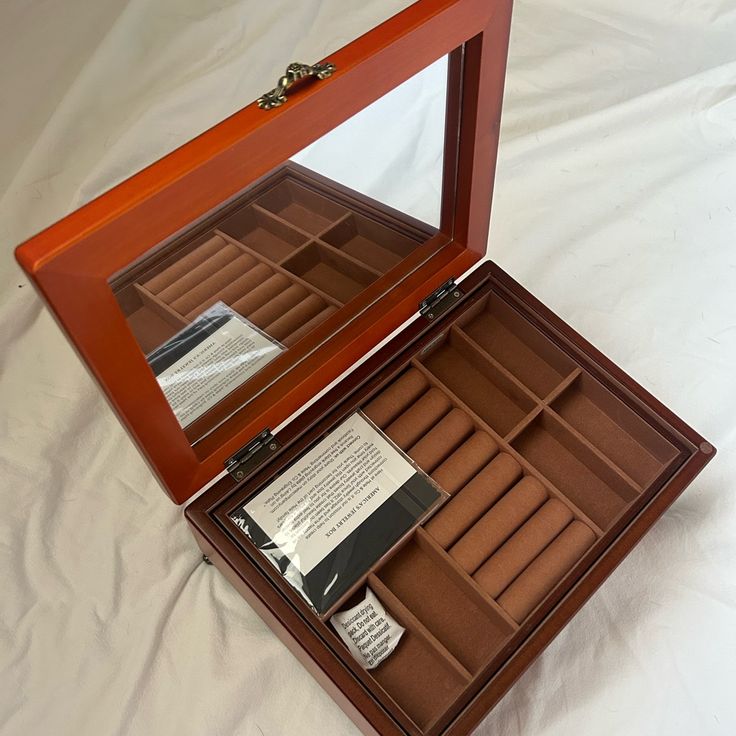 an open wooden watch box sitting on top of a white sheet covered bed with papers in it