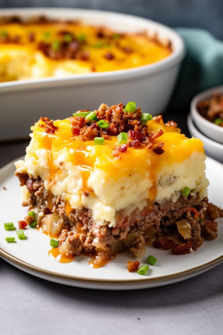 a piece of meat and cheese casserole on a plate with another dish in the background