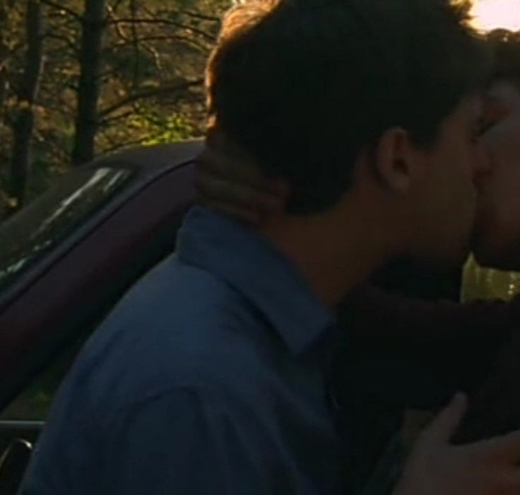 a man and woman kissing in the back of a car with trees in the background