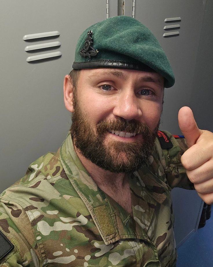 a man with a beard wearing a green beret and giving the thumbs up sign