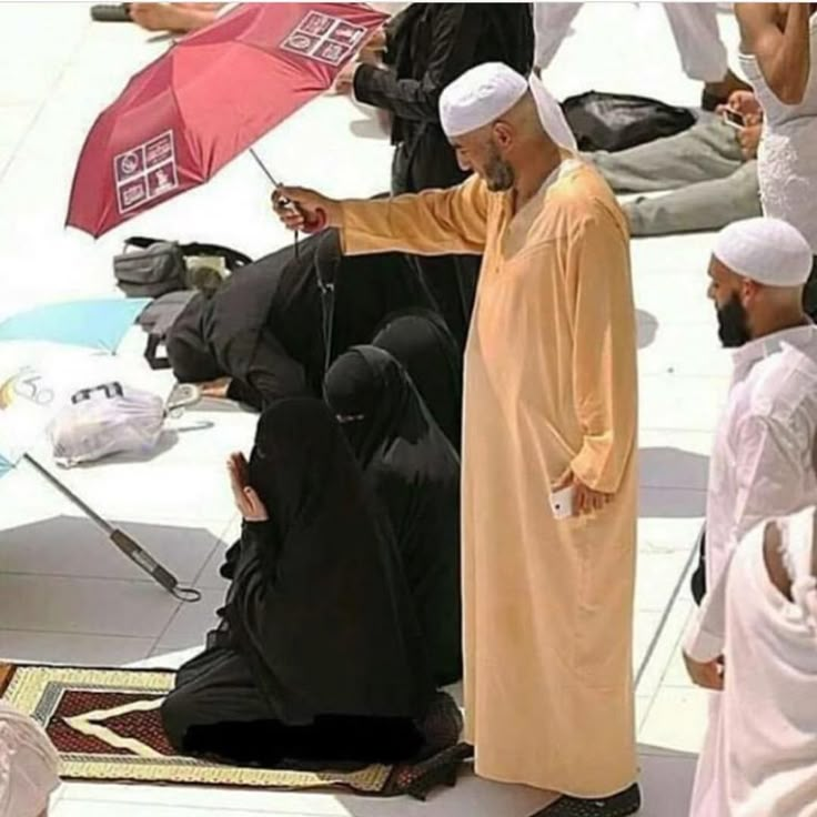 several men sitting on the ground with umbrellas in their hands and one man standing