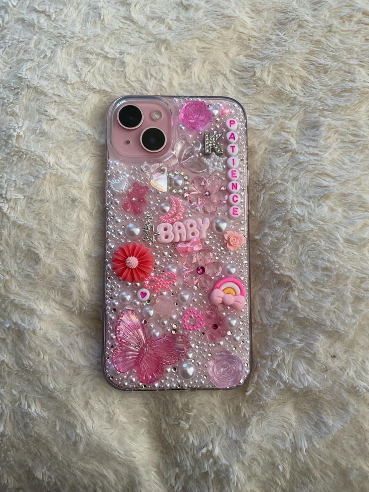 an iphone case with pink flowers and other things on the back, sitting on a fluffy white surface