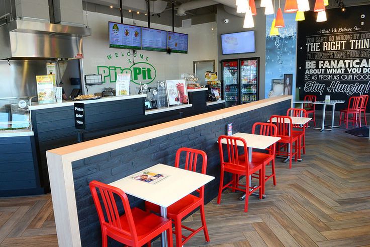 an empty restaurant with red chairs and white counter tops, along with menus hanging from the ceiling