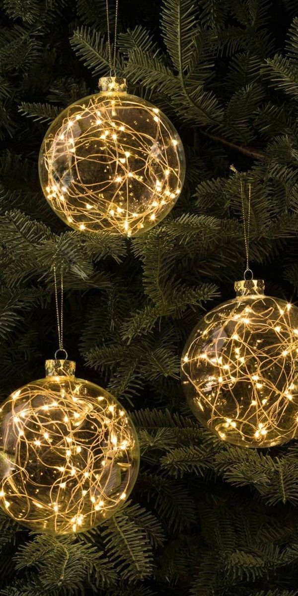 three christmas ornaments hanging from the branches of a tree with lights on them and pine needles