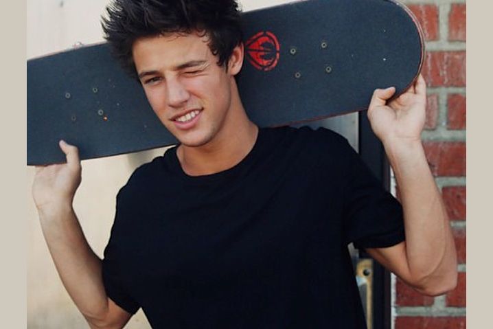 a young man is holding his skateboard over his head and smiling at the camera